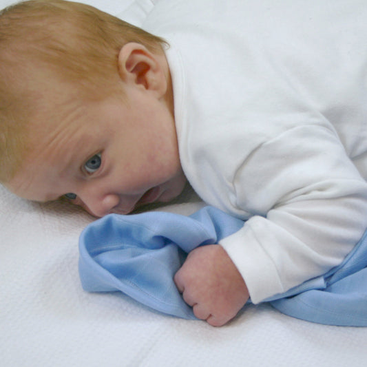 Baby lying on a white surface with a blue blanket