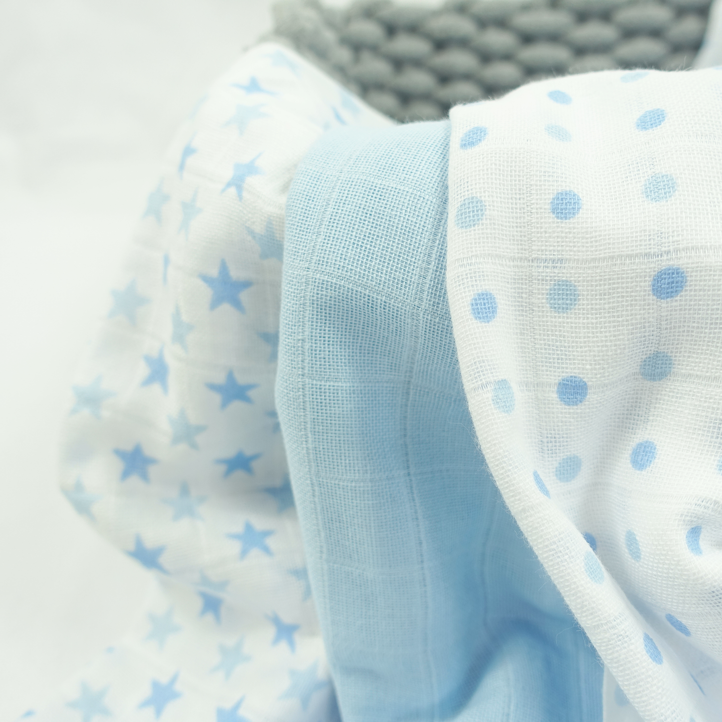 Stack of baby blankets with star and polka dot patterns on a light gray background
