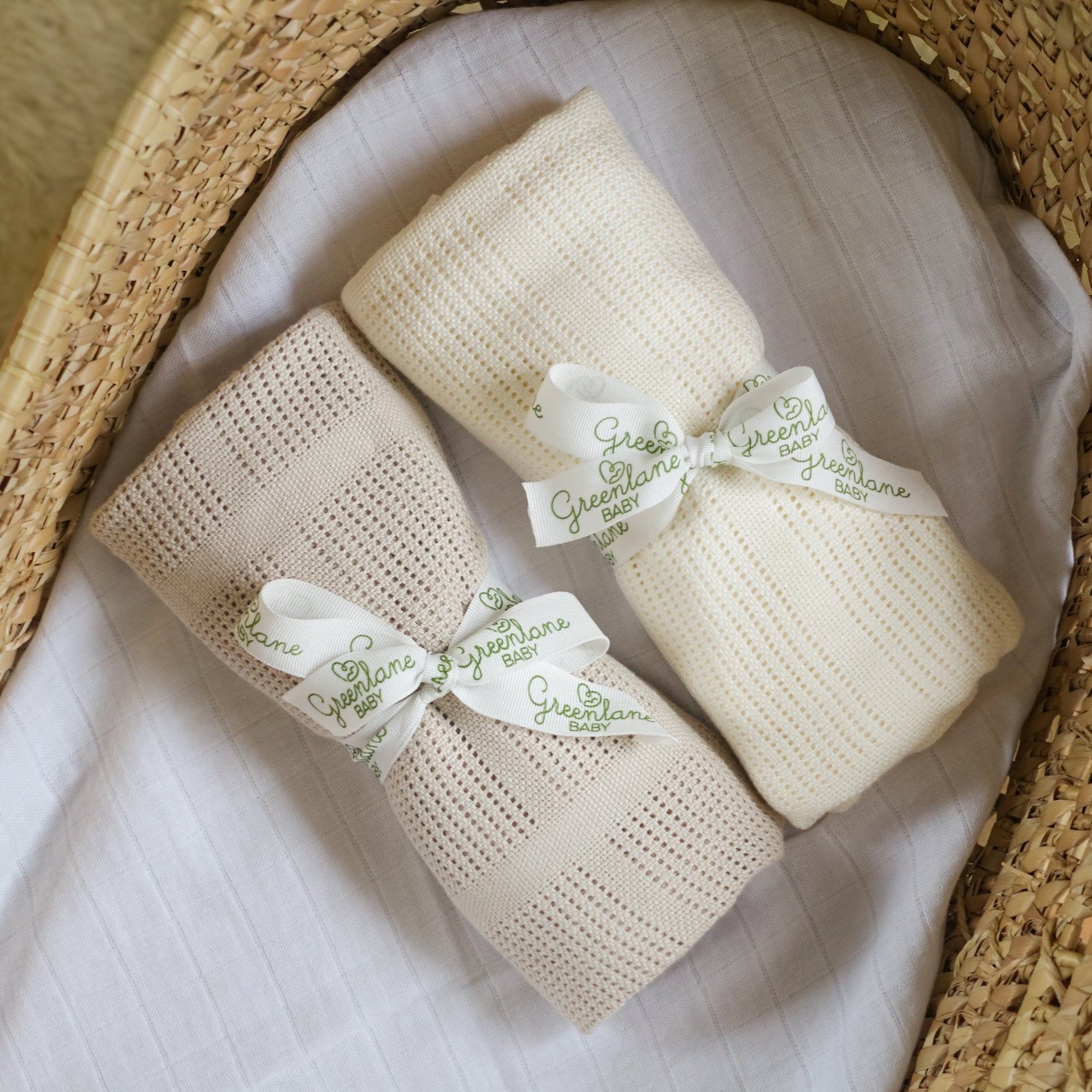 Two beige baby blankets with green text ribbons on a textured surface.