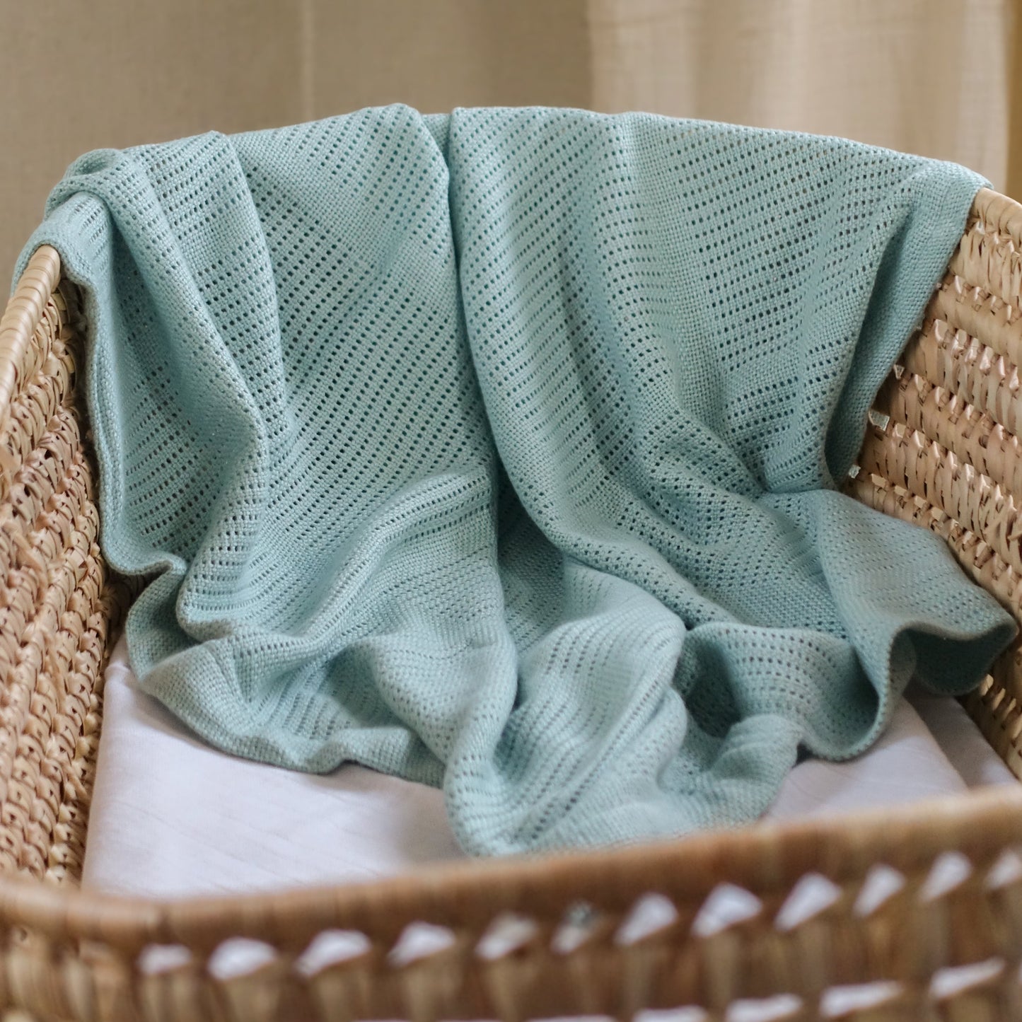 Light green knitted blanket draped over a wicker chair with a neutral background