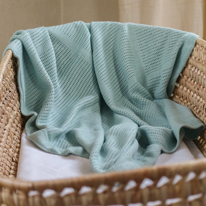 Light green knitted blanket draped over a wicker chair with a neutral background