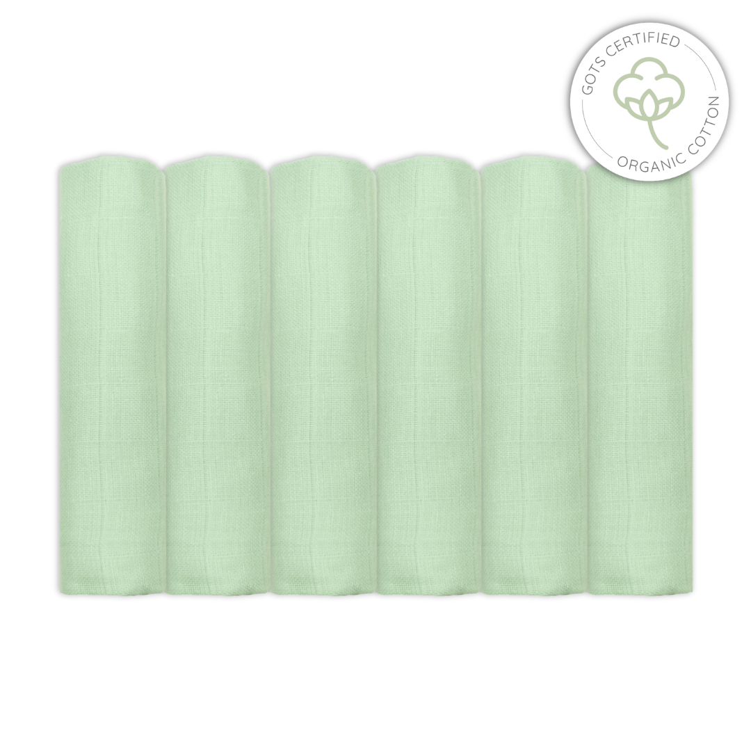 Stack of light sage green baby muslin swaddles with Organic Cotton certification logo on a white background
