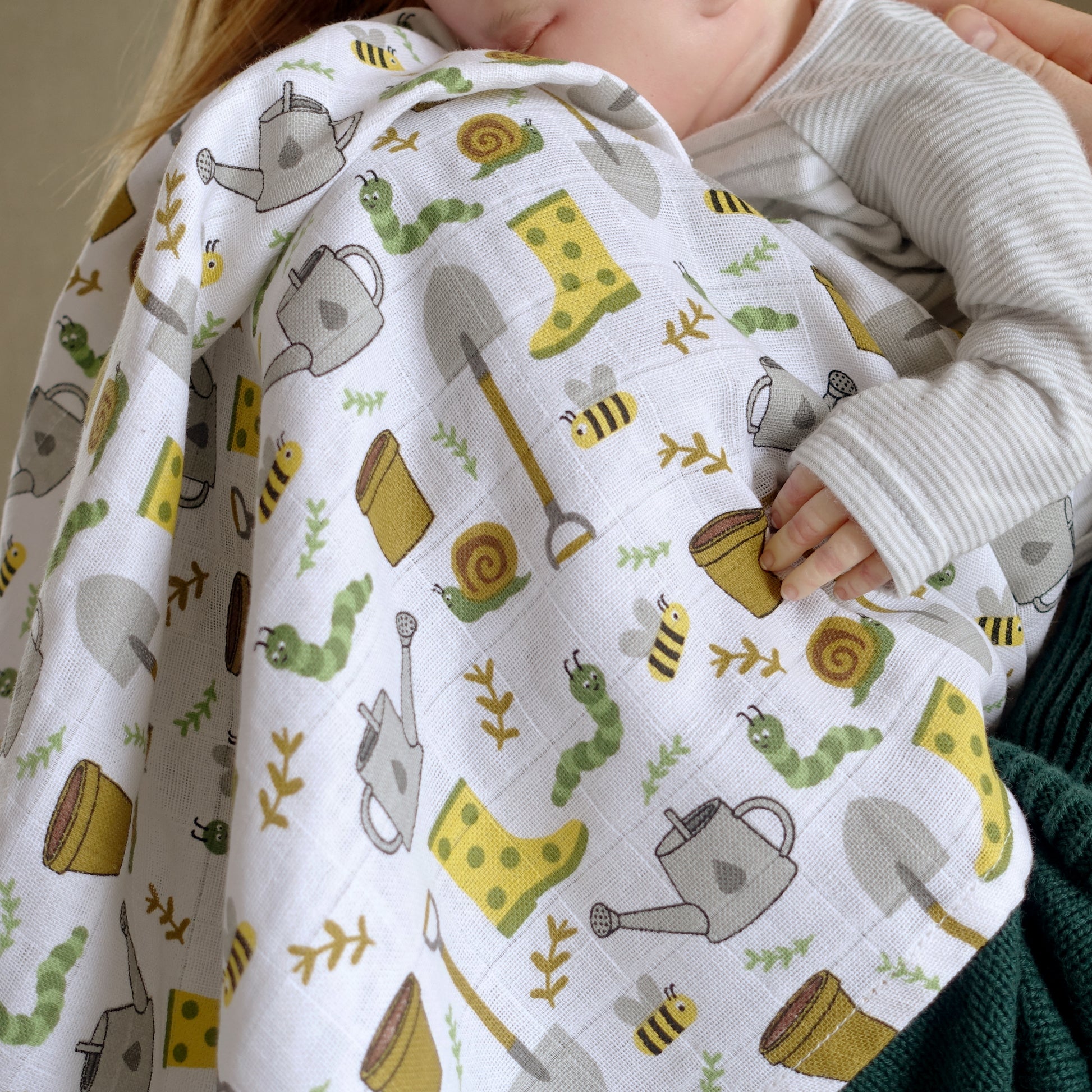 Baby wrapped in a quilt with gardening-themed pattern, held by an adult.