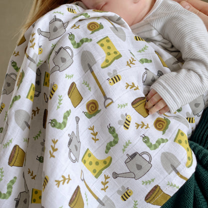 Baby wrapped in a quilt with gardening-themed pattern, held by an adult.