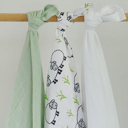Two baby swaddle blankets, one green and one with sheep design, hanging on a wooden rod against a white background.