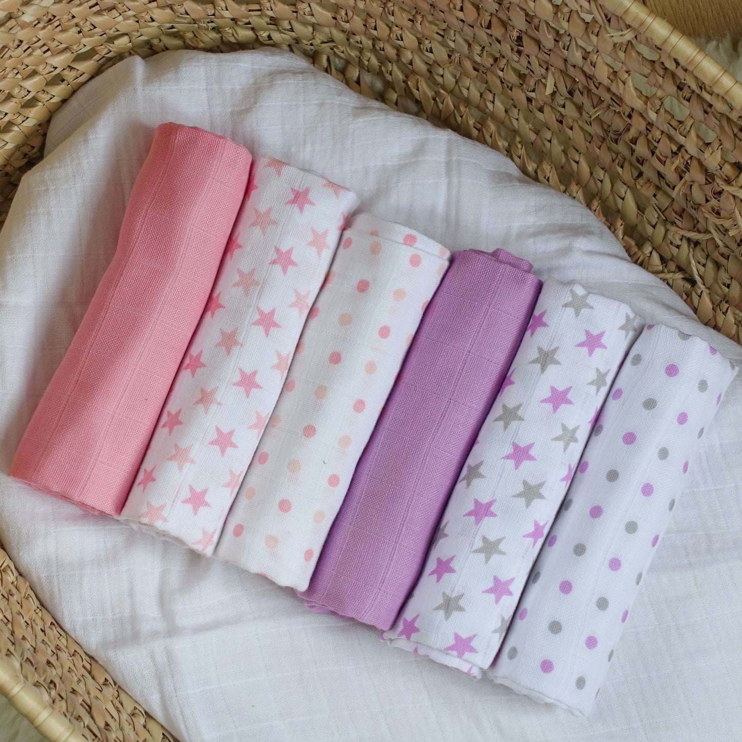Set of folded fabric swatches with star and polka dot patterns in pink, white, and purple on a woven basket background.