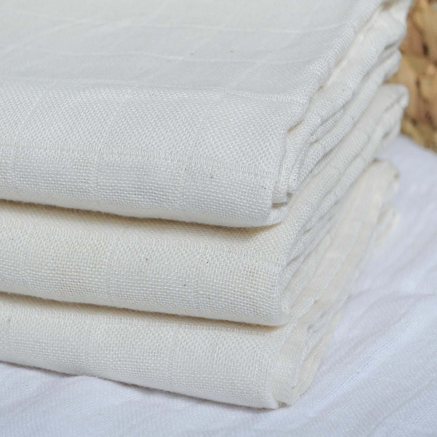 Stack of white towels on a light surface with a woven basket in the background