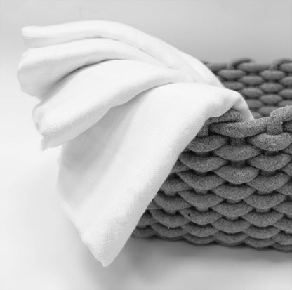 White bamboo muslin swaddle towel draped over a gray woven basket on a light gray background
