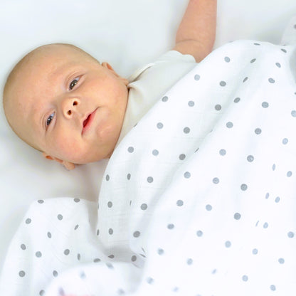 Baby wrapped in a white blanket with gray polka dots on a white background